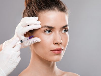 Attractive woman getting beauty injection, grey background